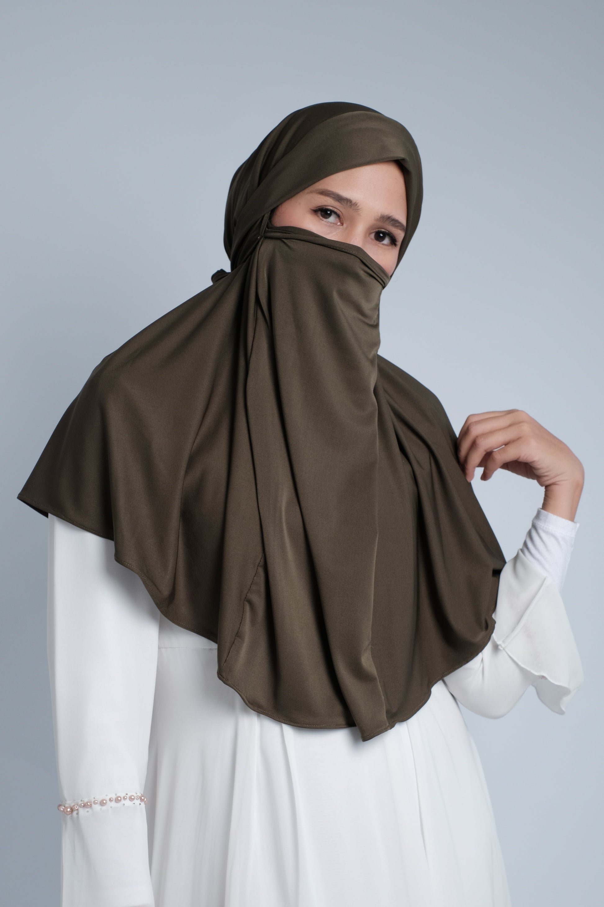 Sister wearing army green jersey khimar with built-in niqab panel; lightweight, breathable fabric offering full coverage for prayer and modest everyday wear.